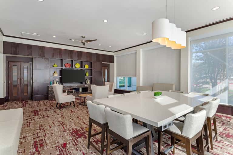 Modern dining and living space with white table, cream chairs, dark wood cabinetry, and large windows overlooking grounds