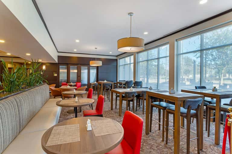 Contemporary lounge area with red accent chairs, round tables, large windows, and warm lighting from pendant fixtures