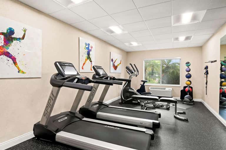 Modern fitness center with treadmills, exercise bikes, colorful motivational wall art, and windows