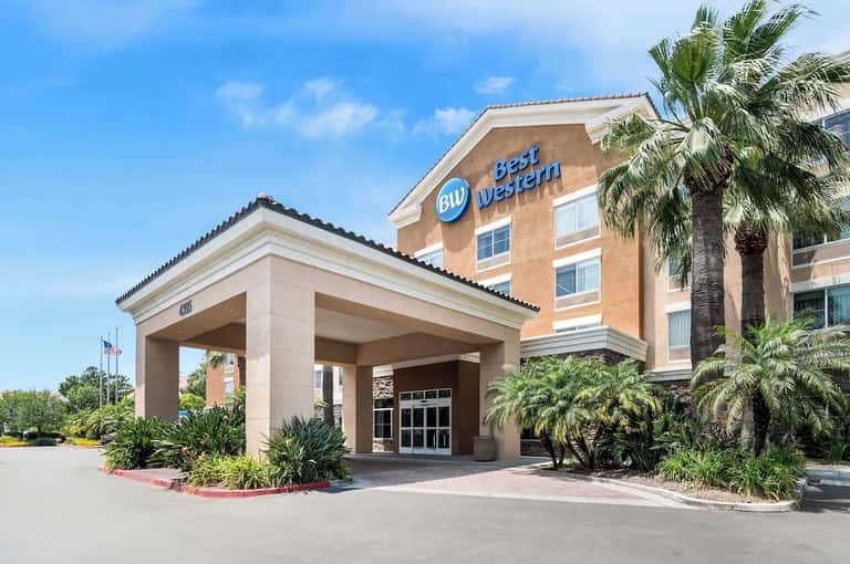 Best Western hotel exterior with tan brick, covered entrance, palm trees, and clear blue sky