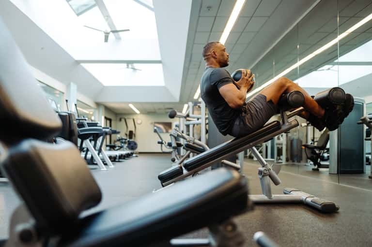 Man doing weighted abdominal exercises on machine in bright, modern gym