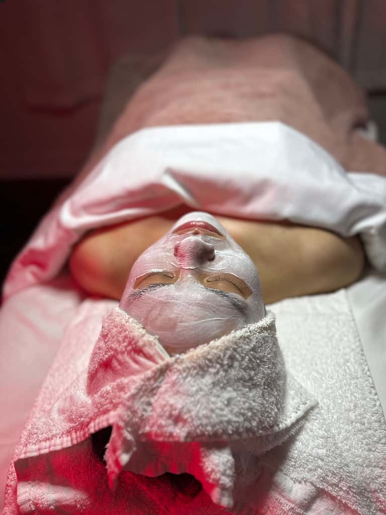 Close-up of client's face with white spa treatment mask applied, relaxing on massage table