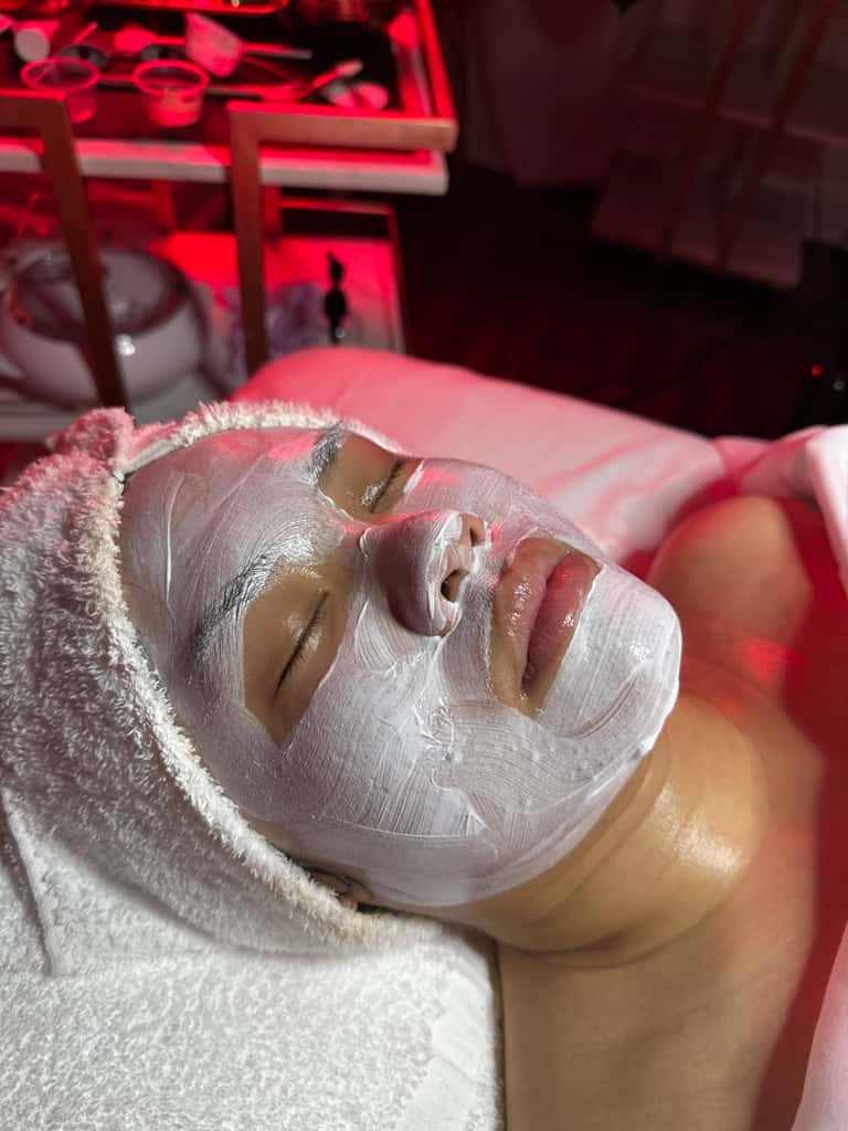 Close-up of white spa facial mask applied to client's face during treatment under red lighting