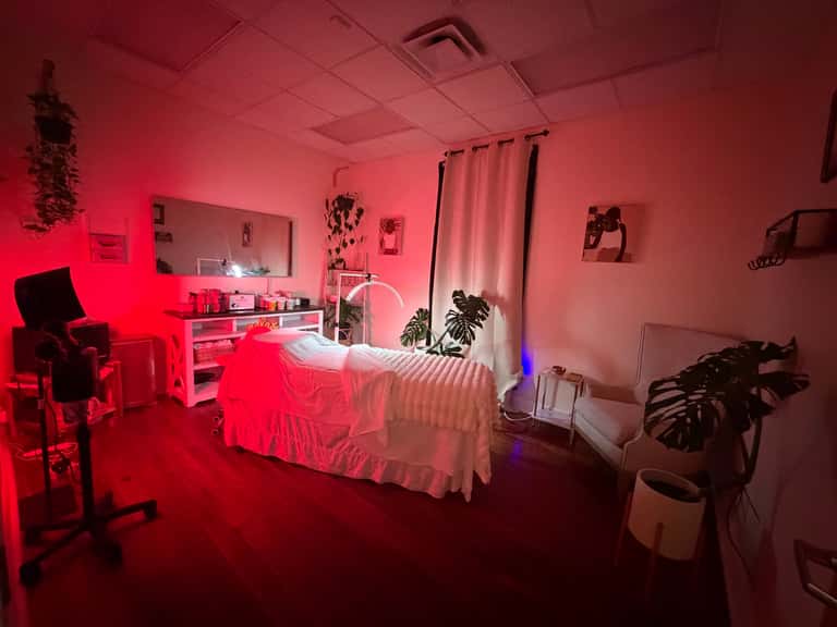 Full spa treatment room with red neon lighting, massage bed, vanity, plants, and modern décor