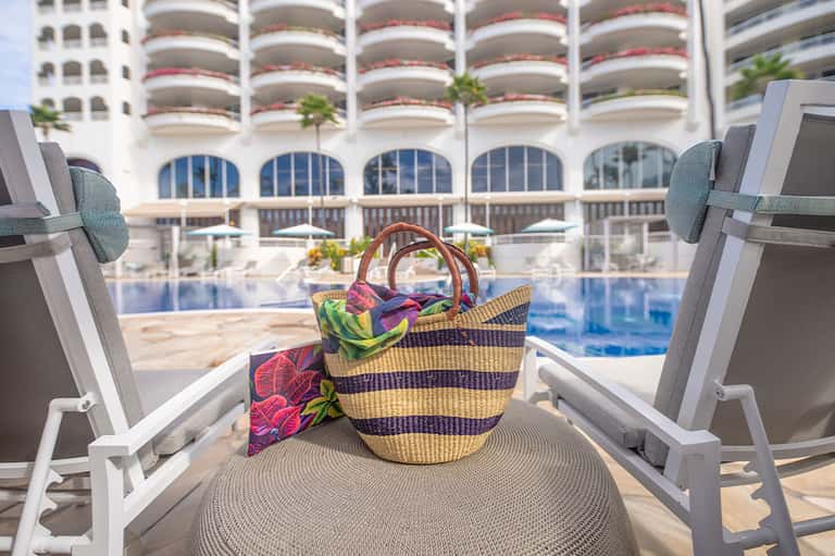 Colorful beach bag and towel on lounge chair overlooking resort pool and ocean