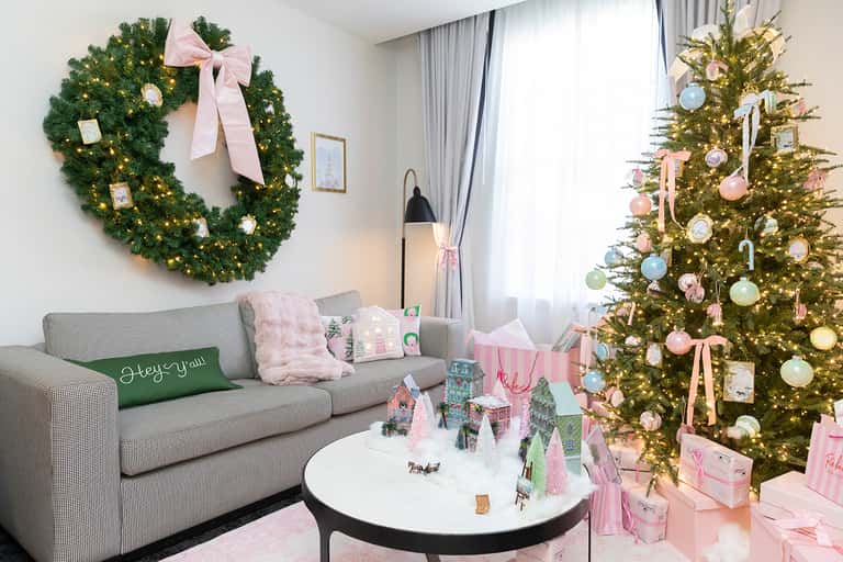 Elegant living room decorated for Christmas with gold tree, pink ornaments, green wreath, and gray sofa