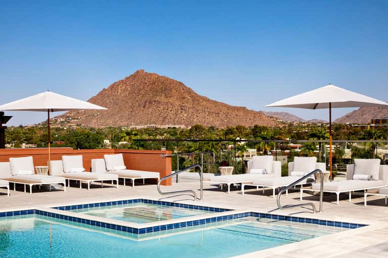 Resort pool deck with white loungers, umbrellas, and mountain backdrop