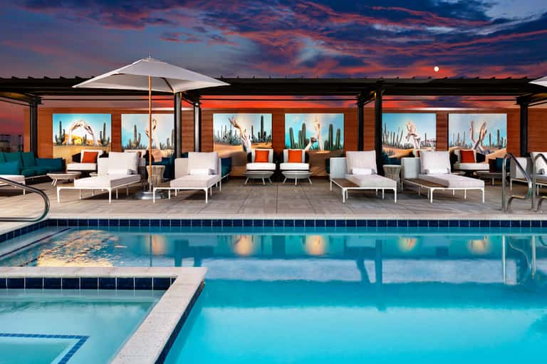 Luxurious resort pool deck at sunset with loungers, umbrellas, and covered seating area overlooking desert landscape