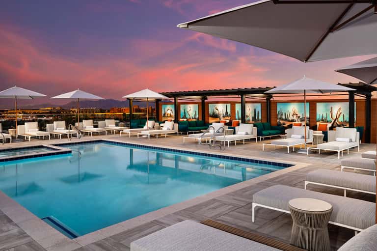 Modern rooftop pool deck at sunset with white loungers, umbrellas, and mountain views