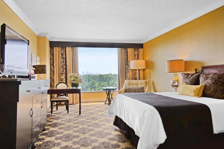 Luxury hotel bedroom with yellow walls, city views, dark wood furnishings, and elegant bedding