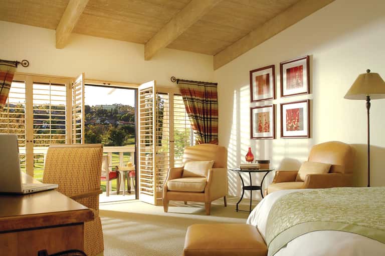 Luxury bedroom with wooden ceiling beams, balcony view, seating area, and warm earth tones