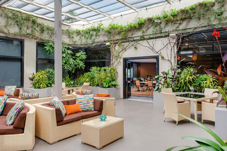 Modern courtyard with woven seating, vibrant cushions, living green walls, and glass ceiling panels