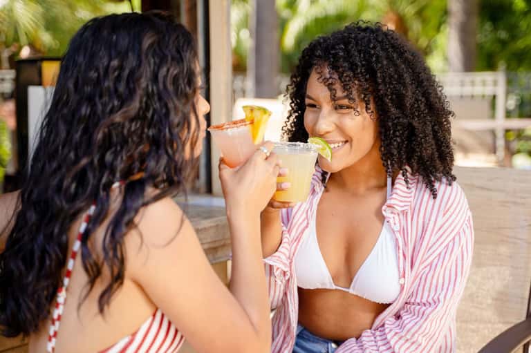 Two women enjoying tropical cocktails outdoors on a sunny day