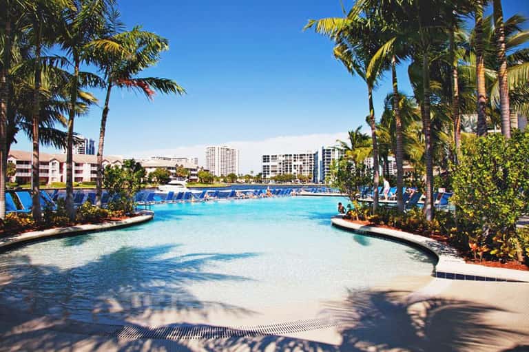 Tropical lagoon-style resort pool with palm trees, lounge chairs, and modern building architecture
