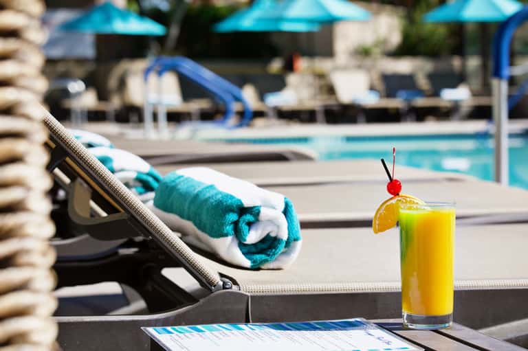 Poolside cocktail with cherry garnish on lounge chair beside turquoise swimming pool