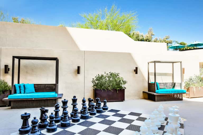 Modern resort courtyard with white canopy daybeds, turquoise cushions, and oversized chess pieces