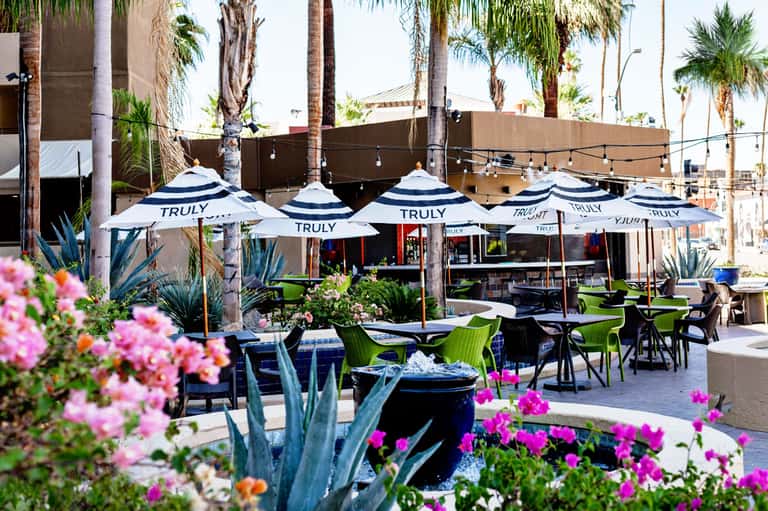 Outdoor dining area with white umbrellas, pink flowers, and modern furniture under palms
