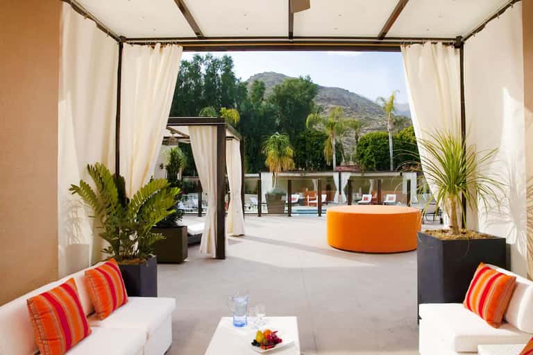 Modern covered terrace with cream curtains, orange seating, mountain views, and pool access