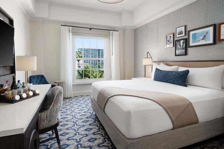 Upscale hotel bedroom with king bed, desk, and floor-to-ceiling windows overlooking city skyline