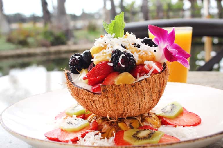 Tropical fruit salad served in coconut bowl with edible flowers and orange juice