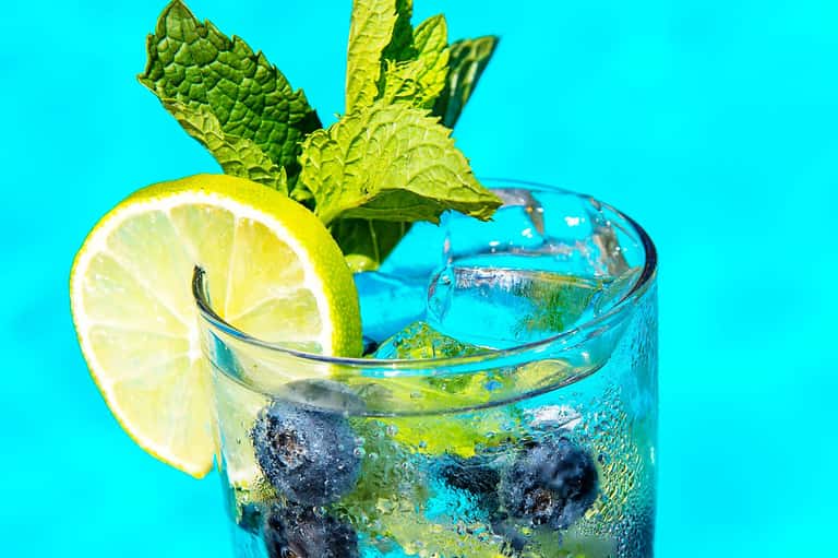 Refreshing mojito cocktail with lime slice, mint leaves, and blueberries on turquoise background
