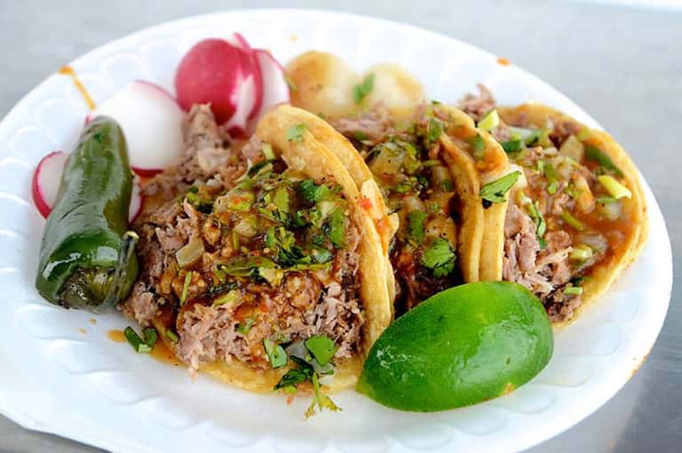 Plate of three shredded meat tacos garnished with cilantro, served with radish slices and lime wedge