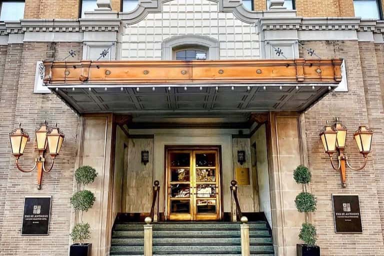 Historic brick hotel entrance with ornate orange awning, brass lanterns, and wooden doors flanked by topiary