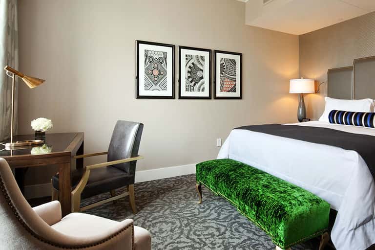 Contemporary hotel bedroom with king bed, desk, and framed artwork on neutral walls