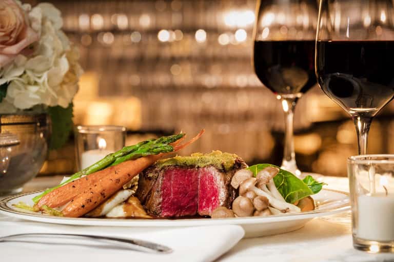 Fine dining plate with rare steak, roasted carrots, mushrooms, and asparagus paired with red wine