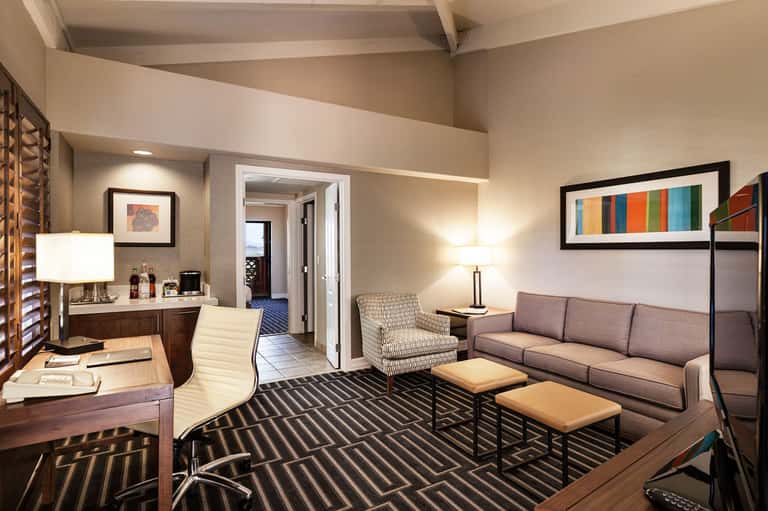 Spacious hotel suite with desk, striped rug, gray sofa, armchair, and modern lighting fixtures