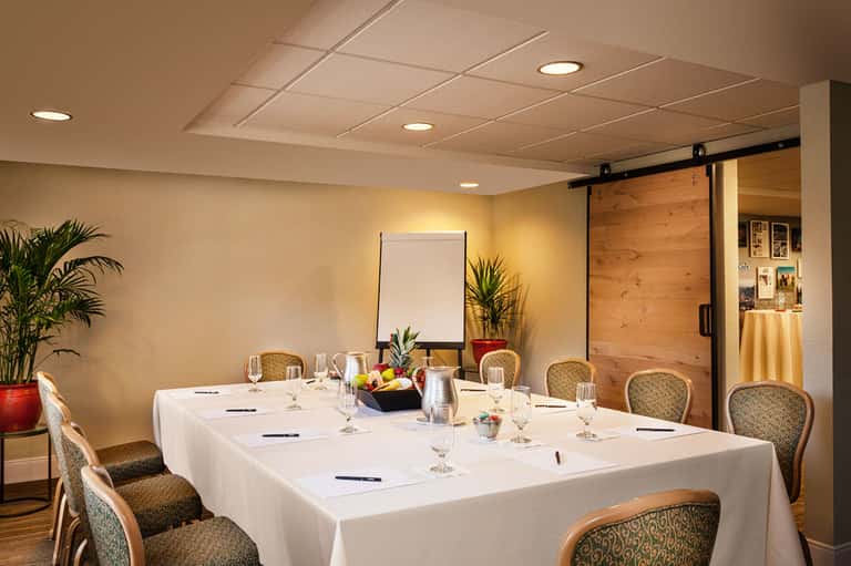 Hotel conference room with white tablecloth dining setup, wooden sliding door, and potted plants