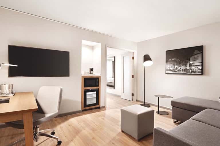 Modern hotel room with desk, TV, sofa, and minimalist furnishings on wooden flooring