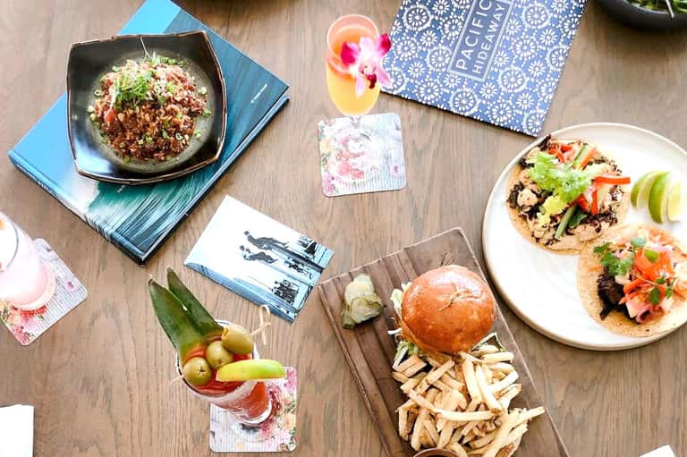 Overhead view of restaurant table with tacos, cocktails, appetizers, and floral menu card