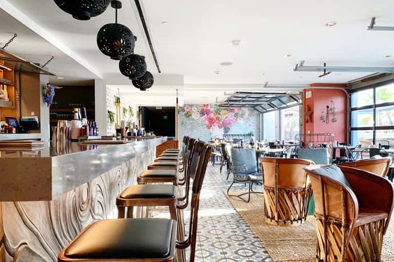 Modern restaurant interior with bar seating, black pendant lights, and pink accent wall