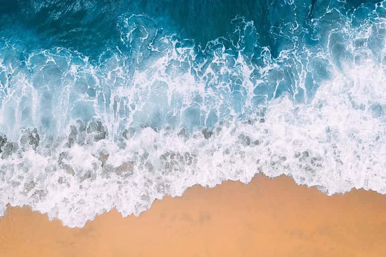 Aerial view of ocean waves crashing on sandy beach