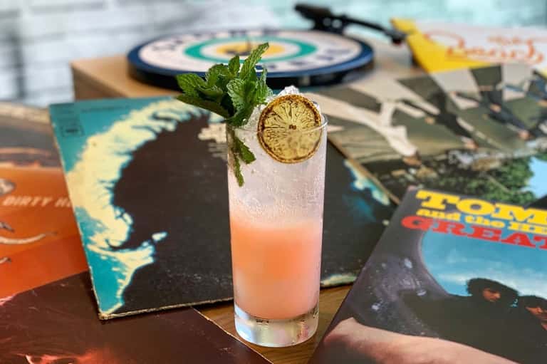 Tropical cocktail with lime slice and mint garnish on colorful magazines beside a dartboard