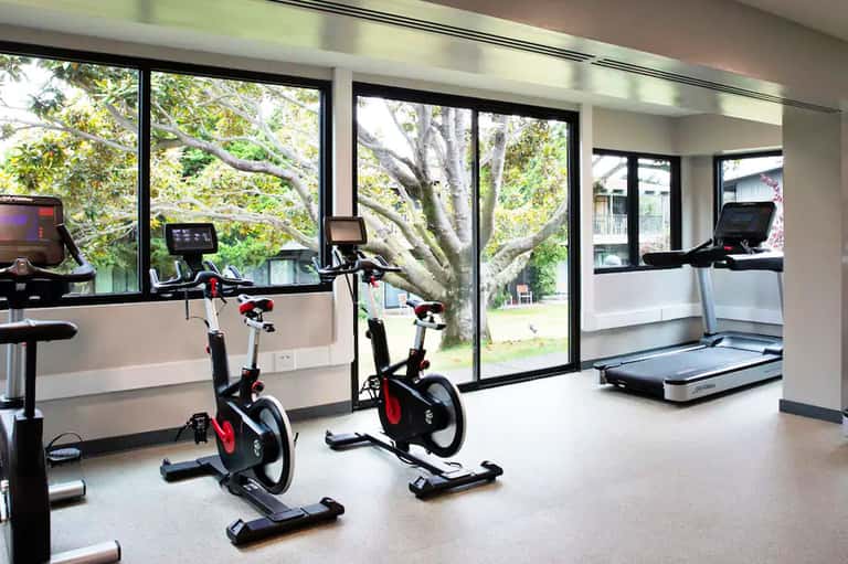 Modern fitness center with stationary bikes, treadmill, and large windows overlooking trees and grounds
