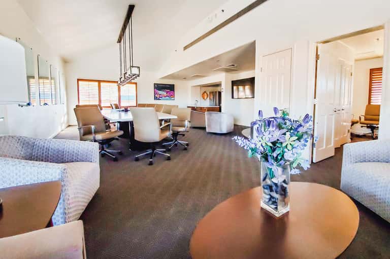 Modern hotel lounge with round table, comfortable seating, flowers, and conference area with large windows