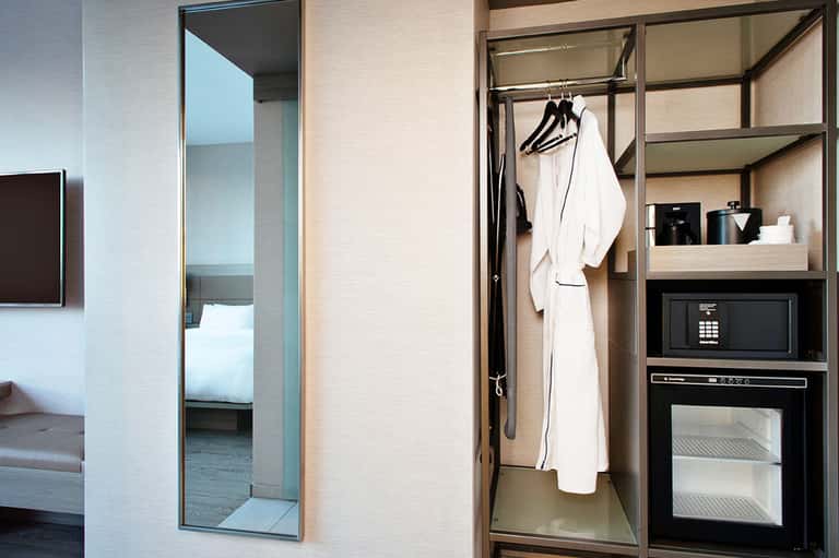 Modern hotel room closet with white robe hanging on dark shelving and microwave