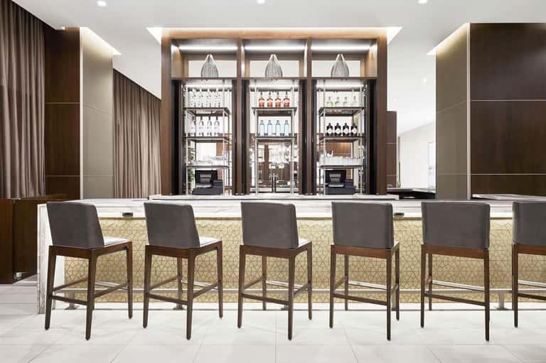 Modern bar with wooden-framed shelving, glass-front refrigerators, and upholstered bar seating