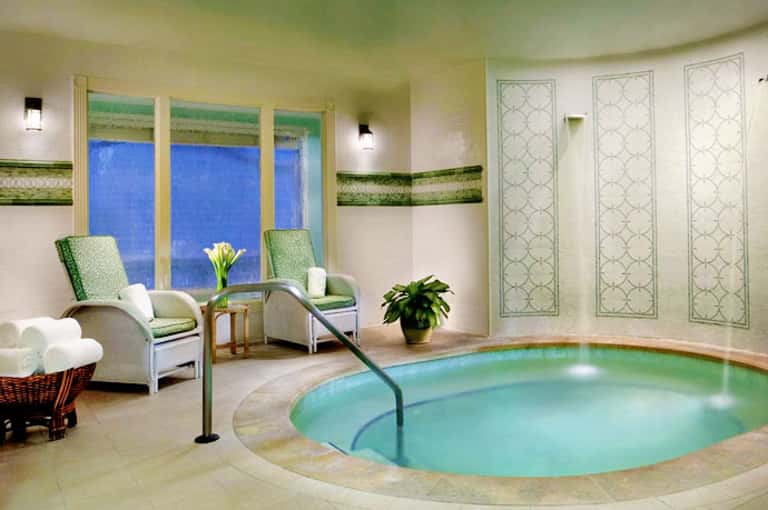 Luxury spa indoor heated pool with aquamarine water, comfortable seating, and floor-to-ceiling windows overlooking blue ocean