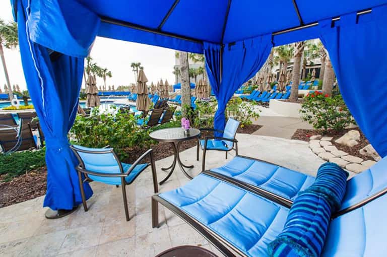 Blue cabana with loungers overlooking beachfront pool and palm trees at resort