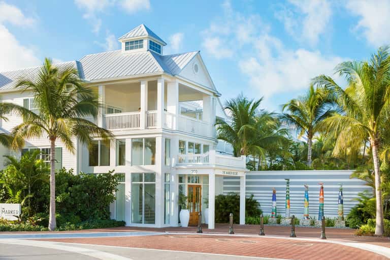 White coastal architecture building with metal roof and palm trees, colorful pole art installation