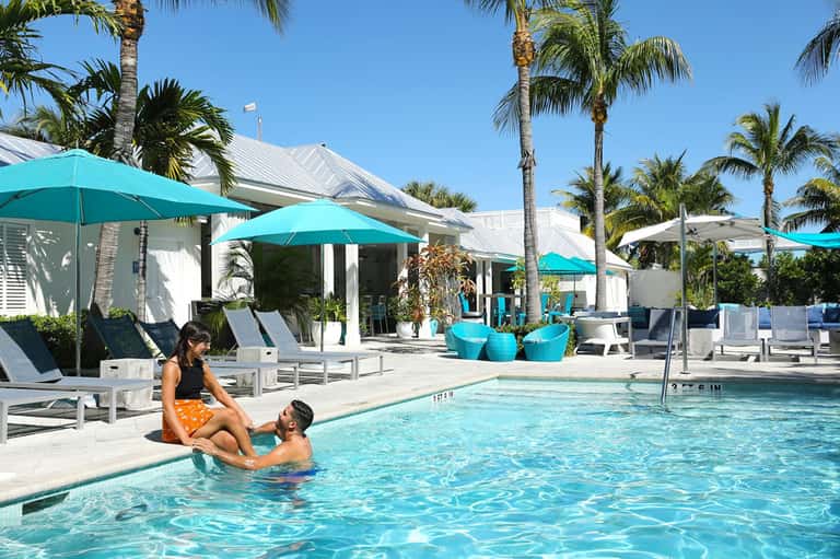 Family enjoying turquoise pool at tropical resort with white cabanas and palm trees under blue sky