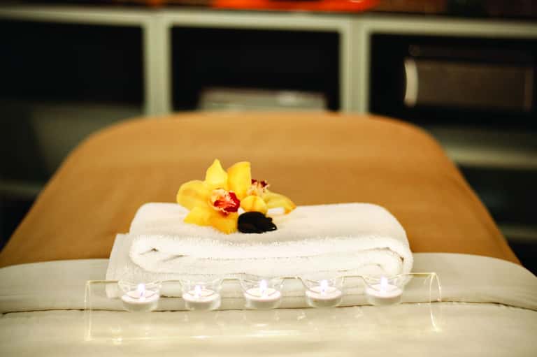 Spa treatment setup with rolled white towel, yellow orchid flower, and lit candles
