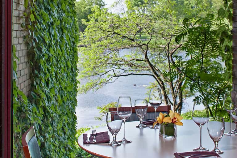 Fine dining table set with wine glasses overlooking water through ivy-covered archway