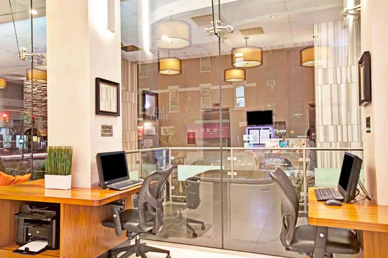 Modern office space with glass partition walls, wooden desks, and ergonomic black chairs