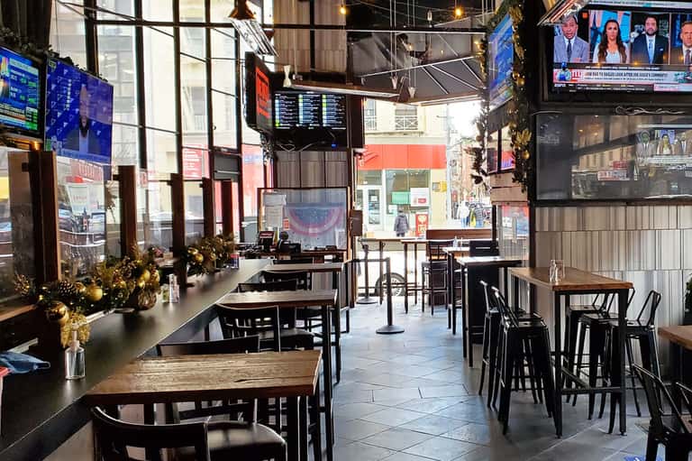 Modern bar interior with black furniture, multiple TV screens, holiday decorations, and street view