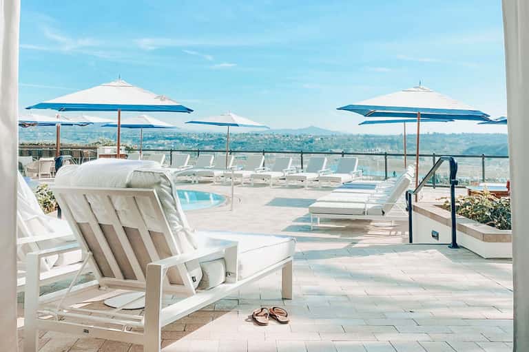 Luxury rooftop terrace with white lounge chairs, blue umbrellas, and panoramic city views