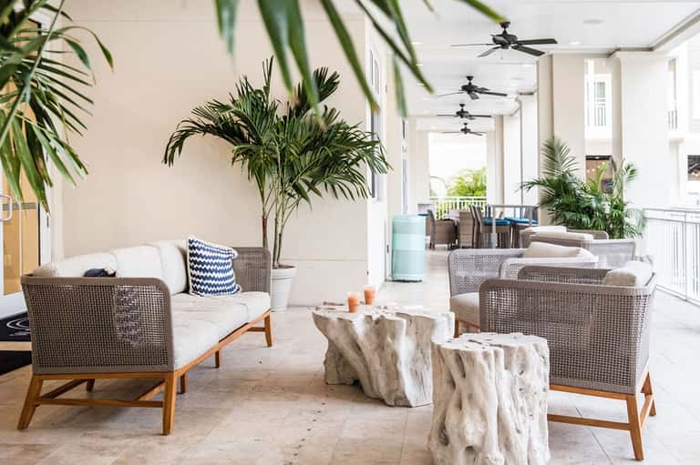 Modern covered patio with woven lounge chairs, potted palm plants, and natural stone accent tables
